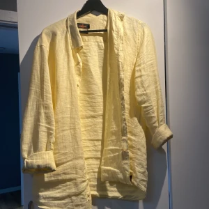 Gul linneskjorta från Morris - Säljer en ljusgul linneskjorta från Morris i storlek S (37/38). Skjortan har klassisk krage, knäppning framtill och långa ärmar. Perfekt för varma dagar och har en avslappnad, stilren look. Kan stryka den innan den skickas om du vill