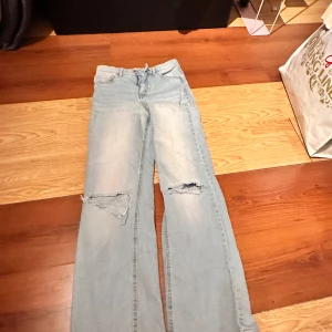 Ljusblå wide jeans med slitningar från LAB Industries - Ljusblå jeans med bred passform och slitna detaljer på båda knäna från LAB Industries. Jeansen har klassisk femficksdesign och är tillverkade i denim. Perfekta för en avslappnad och trendig look.