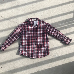 Rutig skjorta i rött, svart och vitt - Snygg rutig skjorta med klassisk krage och knäppning framtill. Skjortan har långa ärmar och ett mönster i rött, svart och vitt. Perfekt för dig som gillar en avslappnad men ändå stilren look.