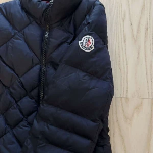  dunjacka från Moncler - Äkta  dunjacka från Moncler med quiltat mönster och hög krage. Jackan har dragkedja framtill och lång ärm. Är i storlek 1 motsvarande S.  Klassisk Moncler-logga på ena ärmen. Varit väl omhändertagen, säljs för 3.000kr nypris ligger ca. 12.000kr