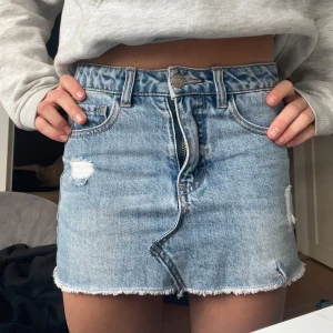 Ljusblå jeanskjol med slitningar - Säljer en ljusblå jeanskjol från Abercrombie & Fitch med rå kant och slitna detaljer framtill. Klassisk femficksmodell med knapp och dragkedja. Perfekt till sommaren!