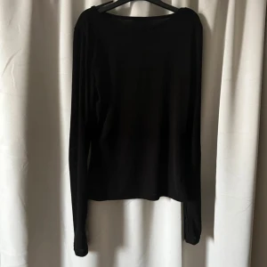 Svart långärmad topp med tumhål - Säljer en svart långärmad topp i tunn och stretchig bomullsblandning. Toppen har tumhål vid ärmsluten vilket ger en sportig känsla. Perfekt att styla till jeans eller kjol för en enkel och clean look.