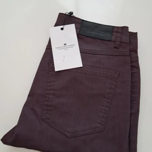 Mörklila byxor från Designers Remix - Säljer ett par mörklila byxor från Designers Remix med klassisk femficksdesign och svarta detaljer. Byxorna är i stretchigt material och har en smal passform som sitter snyggt längs benen. Obs! Str. Ca. 34 (XS) långa (L ca. 34)