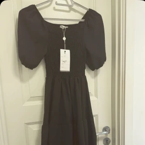 Svart klänning med puffärmar från Paris El-Mai Collection - Supersnygg helt ny svart klänning med puffiga kortärmar och smockad överdel från Paris El-Mai Collection. Klänningen har fortfarande kvar prislappen och är köpt för 400kr och bara testad 