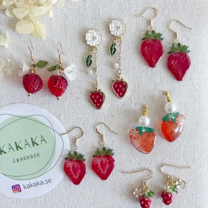 Jordgubbsörhängen från Kakaka - Flera par örhängen med jordgubbstema från kakaka.se. Olika modeller med detaljer som vita blommor, gröna blad, pärlor och guldiga krokar. Färgerna är främst röd, grön, vit och guld. Perfekta accessoarer för dig som älskar söta och unika smycken. Pris: 75-125kr/par + frakt