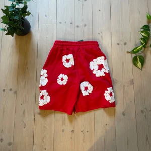 Grå shorts med vita blommor - Grå shorts med resår i midjan och vita blommor tryckta över hela plagget. Mjukt material och avslappnad passform, perfekt för varma dagar.