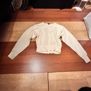 Beige sweatshirt från Gina Tricot - Säljer en enkel och stilren beige sweatshirt från Gina Tricot. Tröjan har rund halsringning, långa ärmar och breda muddar vid ärmslut och nederkant. Perfekt för en avslappnad och snygg look.