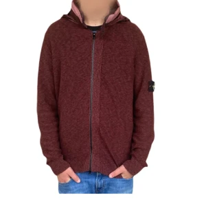 Vinröd hoodie från Stone Island - Säljer en vinröd hoodie från Stone Island med ikonisk patch på vänster ärm. Tröjan har dragkedja framtill, huva med snyggt tyg och ribbade muddar. Perfekt för dig som vill ha en chill och stilren look. Materialet är mjukt och känns skönt mot huden.