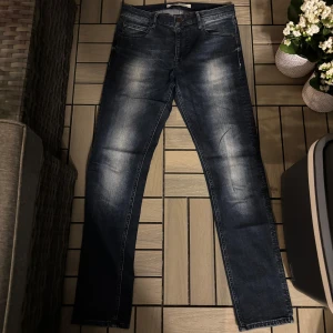Mörkblå skinny jeans med slitningar - Snygga mörkblå jeans med skinny passform och coola slitningar på framsidan. Klassisk femficksmodell med dragkedja och knapp. Jeansen har en tvättad look med ljusare partier på lår och knän, vilket ger en trendig vibe.