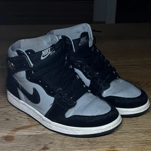 Nike Air Jordan 1 High svart/grå - Jordan 1 retro HI OG. Bra skick. Det svarta är någon typ av päls liknande tyg. Jätte sköna. Priset kan diskuteras