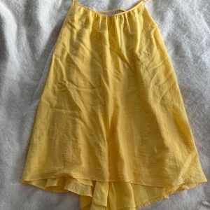 Gul omlottkjol från H&M, storlek S - Säljer en flowy gul omlottkjol från H&M i storlek S. Kjolen har en lätt och luftig känsla med volangdetalj och elastisk midja. Perfekt för soliga dagar och har en mjuk, skrynklig struktur. Materialet är bomull och kjolen har en snygg omlott-design.