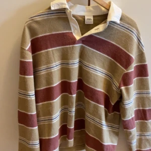 Randig pikétröja från ZARA - Säljer en chill randig pikétröja från ZARA med breda ränder i beige, vinrött och vitt. Tröjan har vit krage, v-ringning och långa ärmar. Perfekt för dig som gillar retrovibbar och vill sticka ut lite extra. Storlek M men passar bättre för dig som har S. Knappt använd 