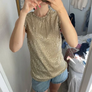 Beige glittrig leopardmönstrad blus - Supersöt beige blus med glittrigt leopardmönster och volangdetaljer vid ärmslut och halsringning. Tunn och luftig med ärmlös design, perfekt för varma dagar när du vill sticka ut lite extra.