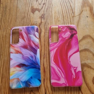 Färgglada mobilskal med mönster till samsung galaxy s 21 - Två snygga mobilskal med unika mönster. Ena skalet har ett färgstarkt fjädermönster i blått, lila och rosa toner, medan det andra har ett abstrakt rosa och rött mönster. Perfekt för dig som vill ge mobilen en personlig touch.