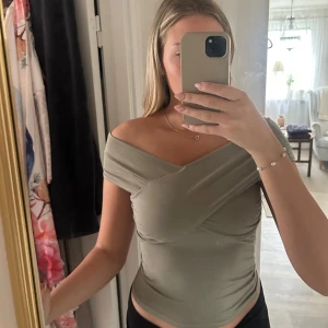 Offshoulder topp Gina - Säljer en olivgrön omlott topp från Gina Tricot i storlek S. Modellen är offshoulder med snygg omlott-effekt och draperade detaljer framtill. Tunn och mjuk, stretchig bomullsmix som sitter tight och framhäver figuren. Perfekt för dig som gillar trendiga och stilrena plagg.