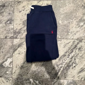 Mörkblå mjukisbyxor Polo Ralph Lauren - Snygga mörkblå mjukisbyxor från Polo Ralph Lauren med klassisk röd logga broderad på höften. Byxorna har resår i midjan och sidofickor, perfekta för chill eller träning. Mjukt material som känns skönt mot huden.