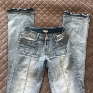 Bootcut  ljusblå lågmidjade jeans - Säljer ett par ljusblå jeans från Madlady med utsvängda ben, uppsprättade längst ned. Jeansen har framfickor med markerade sömmar och bakfickor med lock och knapp. Dubbelknäppning fram och klassisk jeanslook. 