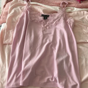 Ljusrosa linnetopp med spets från Amisu - Supersöt ljusrosa linnetopp från Amisu med tunna axelband och v-ringning dekorerad med spets. Toppen har en mjuk och flowy känsla, perfekt för att lyfta vilken outfit som helst. Snygg att styla med jeans eller kjol för en trendig look.