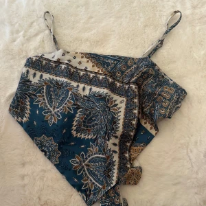 Mönstrad blå linnetopp från SHEIN - Snygg linnetopp från SHEIN i storlek XL med tunna axelband och knyt framtill. Toppen har ett paisleyinspirerat mönster i blått, vitt och brunt, och är gjord i ett mjukt, glansigt polyestermaterial. Perfekt för att ge din outfit en boho-vibe.