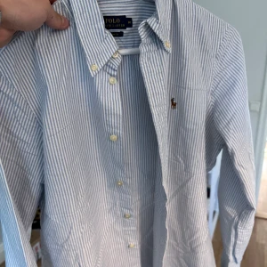 Ralph lauren skjorta  - En vit/blå randig Ralph Lauren skjorta i väldigt bra skick. Inga fläckar eller skador. Skjortan är storlek M men är lite kort på mig och är 184cm och väger 70kg. 