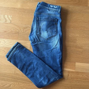 Dondup George - Säljer ett par Dondup George jeans i blå tvätt med slitna detaljer och hål på benen. Skinny fit med klassiska fem fickor och dragkedja. Snyggt blekta partier och små färgstänk ger en cool och unik stil!