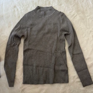 Grå ribbad polotröja från Primark - Säljer en grå ribbad polotröja från Primark i storlek L. Tröjan har lång ärm och en högre krage som ger en clean och stilren look. Materialet är mjukt och stretchigt, perfekt för lager-på-lager under kyliga dagar. Passar dig som gillar enkel och snygg stil.