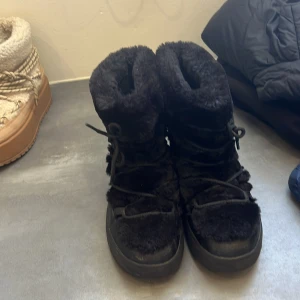  Vinterskor  - Säljer ett par svarta vinter skor med fluffigt pälsmaterial och snörning framtill. Skorna har en platt sula och hög skaft som håller dig varm under kalla dagar. Perfekta för vinter och snö, riktigt mysiga och coola att glida runt i. från din sko i storlek 37 passar perfekt i vintern och as snygga
