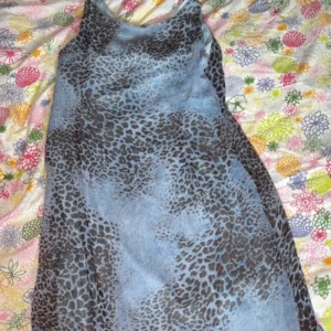 Blå leopardmönstrad långklänning - Säljer en blå långklänning med leopardmönster och tunna axelband. Klänningen har en flowy passform och är perfekt för dig som gillar djurprint och vill sticka ut. Materialet känns lätt och svalt, vilket gör den skön att bära under varma dagar.