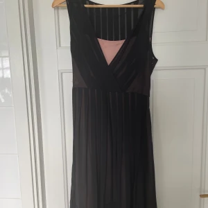 Svart cocktailklänning från Esprit - Snygg svart cocktailklänning från Esprit med transparenta ränder. Klänningen är ärmlös och har ett ljusrosa foder som syns vid halsringningen. Dragkedja på sidan och knytbart skärp. Tillverkad i polyester, perfekt för dig som gillar stilrena och eleganta plagg med lite edge.