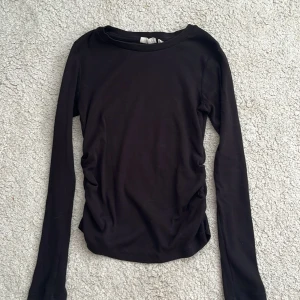 Svart långärmad topp i bomull  - En svart, enkel och stilren långärmad topp med rund hals. Materialet är mjukt och stretchigt, troligtvis bomull. Passformen är normal och toppen är perfekt att styla med jeans eller kjol. Snygg att ha som lager eller bara som den är.