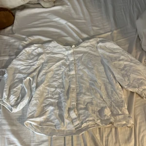 Vit linneskjorta med knappar, M - Snygg vit skjorta i linnemix med klassisk krage och knappar framtill. Långärmad modell med elastiska muddar vid ärmslut. Perfekt för dig som gillar en clean och chill stil. Passar dig som vill ha en luftig och enkel skjorta till sommaren.