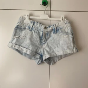 Ljusblå low rise jeansshorts från Hollister - Säljer ett par ljusblå jeansshorts från Hollister, modell short-short med låg midja. De har slitna detaljer framtill, klassiska fickor och uppvikta benslut. Perfekt för dig som gillar en chill och avslappnad stil på sommaren. Storlek w25, 36cm rakt över midjan. Använd gärna prisförslag!
