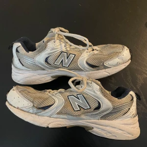 Trendiga New Balance 530 sneakers vit/mörkblå strl 41,5 - Säljer ett par New Balance 530 sneakers i vit och grå mesh med detaljer i mörkblått. Storlek 41,5, använt skick syns på bilderna. Klassisk chunky siluett med ABZORB-dämpning och ventilerande material. Perfekt för dig som gillar retrostil och sportig vibe. Obs! Finns 3 små hål se bilder 