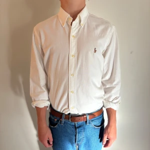 Vit skjorta från Polo Ralph Lauren - Vit klassisk skjorta från Polo Ralph Lauren med broderad logga på bröstet. Skjortan har långärmad design, knappar framtill och button-down krage. Tillverkad i mjuk bomull som känns skön mot huden. Perfekt för dig som gillar stilrena och tidlösa plagg. Modellen är 177 och väger 64kg! (Plagget skickas inom 24 h efter det köpts)! Hör av dig vid frågor.
