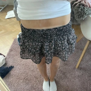 Svart blommig volangkjol - Svart kjol med blommor på! Andvänd fåtal gånger men som ny!