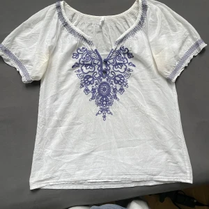 Vit blus med blå broderi från Sisters - Supersöt vit blus från Sisters i storlek 36, med detaljerat blått broderi framtill. 💙💙Desvärre har den missfärgningar. 