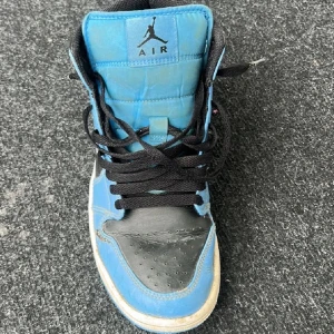 Nike Air Jordan 1 blå/svarta sneakers storlek 41 - Säljer ett par Nike Air Jordan 1 sneakers i blått och svart med klassisk high-top siluett. Skorna har svart snörning, rund tå och vit sula. Ikonisk Air Jordan-logga på sidan och Swoosh i blått. Tillverkade i skinn med meshfoder för extra komfort. Är lite smutsiga och trasiga men annars är dom helt perfekta 