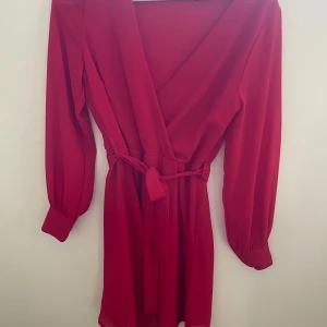 Röd omlottklänning  - Röd omlottklänning från Sisters Point med långa ärmar och knytband i midjan. Klänningen har v-ringning och är i en kort modell! Superfin sommarklänning 