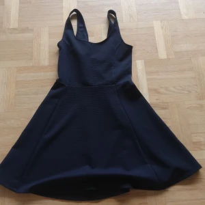 Svart kort klänning från H&M Divided - En svart, ärmlös kortklänning från H&M Divided i storlek 38. Klänningen har breda axelband, figurnära överdel och utställd kjol som ger en snygg siluett. Perfekt för varma dagar😍 