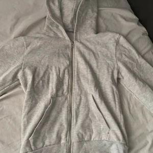 Ljusgrå hoodie med dragkedja - Ljusgrå hoodie från lager157 i storlek S. Tröjan har huva, hel dragkedja framtill och två stora fickor. Mjuk insida i fleece och klassisk passform, perfekt för chill dagar eller när du vill vara extra bekväm. Knappt använd.