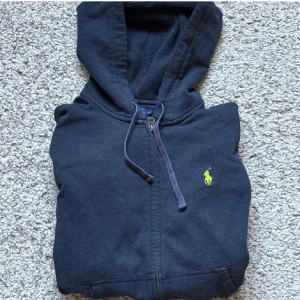 Polo Ralph Lauren zip hoodie - Snygg mörkblå hoodie i XS från Polo Ralph Lauren med dragkedja och huva. Tröjan har snörning i huvan och den klassiska gula broderade loggan på bröstet. Perfekt för en chill och stilren look.
