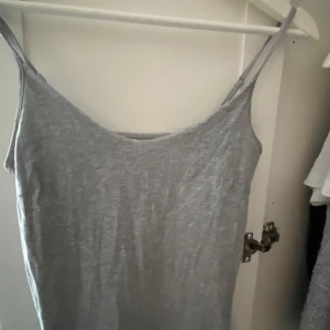 Grå linne - En enkel och stilren grå linne med smala axelband och ärmlös design. Linnet har en rak passform och är tillverkad i mjukt material, perfekt för varma dagar eller att styla med en jacka.