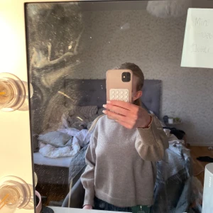 Beige stickad tröja med breda muddar - En beige stickad tröja med rund hals och breda ribbade muddar vid ärmslut och nederkant. Tröjan har en loose passform och är perfekt för lager-på-lager. Enkel och stilren design som funkar till allt.
