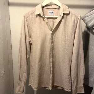 Beige linneskjorta Only & Sons  - Stilren beige skjorta från Only & Sons. Skjortan är tillverkad i svalt linne, har klassisk krage, långa ärmar och knäppning framtill. Perfekt för dig som gillar en clean och enkel look med lite mer edge.