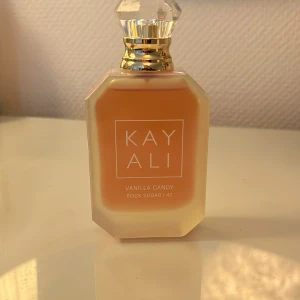 Kayali Vanilla Candy Rock Sugar 42 - Kayali Vanilla Candy Rock Sugar 42 är en eau de parfum i en lyxig, frostig glasflaska med guld- och kristalldetaljer. Doften har noter av sockrad päron, söt viol, bubbelgum, vit kola, rock sugar och vaniljkräm. Flaskan rymmer 50 ml och har en modern, oktagonal form. Endast använd ett fåtal gånger, har dofter i liknade stil så därav att de är till salu.