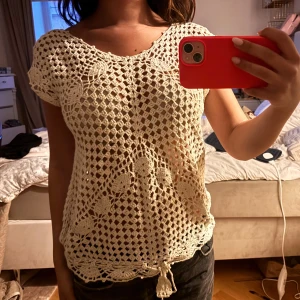 Beige virkad blus med knyt - Superfin beige virkad blus med korta ärmar och snygg knytning nertill. Blusen har ett genombrutet mönster med virkade blommor och lövdetaljer, perfekt för lager-på-lager och somrig vibe. Lätt och luftig, passar till både jeans och kjol. Det står tyvärr ingen storlek på.