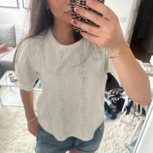 Vit blus med broderade vågmönster - Superfin vit blus med korta ärmar och vågiga broderade detaljer framtill. Blusen har rund halsringning och är gjord i ett lätt, luftigt tyg som känns perfekt för varmare dagar. Knappt använd.