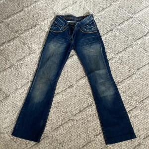 Blå Morgan Jeans med broderade fickor - Snygga blå jeans från Morgan med coola broderade bakfickor i orange. Jeansen har klassisk femficksdesign, dragkedja och raka ben. Färgen är mörkblå med slitningar för en trendig look. Perfekta för dig som gillar streetstyle och detaljer.