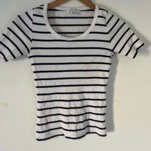 Randig ribbad t-shirt från Amisu - Snygg vit ribbad t-shirt från Amisu med svarta horisontella ränder. Modellen är kortärmad och har en rund halsringning. Perfekt för dig som gillar en klassisk men trendig stil.