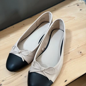 Ballerinaskor H&M - Snygga ballerinaskor i beige med svart tå från H&M. Helt slutsålda på H&Ms hemsida. Storlek 38, true to size. Några små skavanker som visas på bild men inget som syns tydligt.